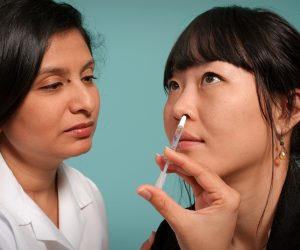 woman administering a nasal medicine to a patient