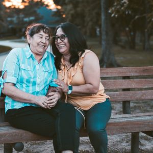 two women sitting on a park bench laughing together