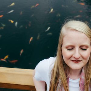 woman standing in front of a fish pond with eyes closed