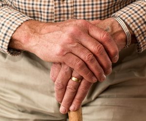 old man's hands resting on top of a walking cane
