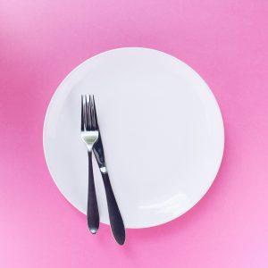 empty white plate with silverware against a pink backdrop